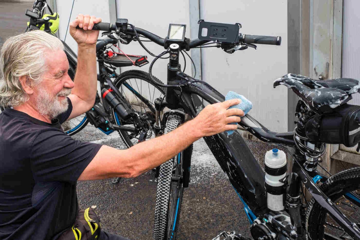 Man cleaning an e-bike frame with a soapy sponge, demonstrating safe washing technique without a pressure washer