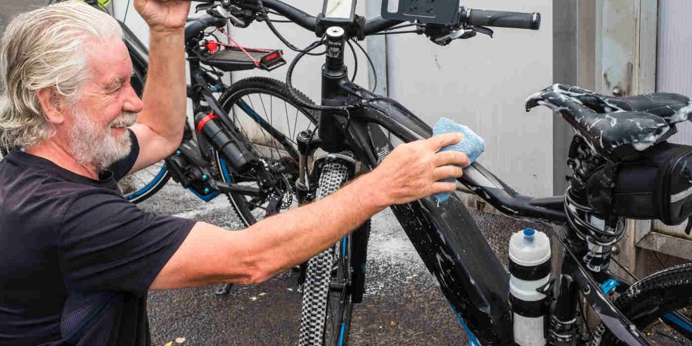 Man cleaning an e-bike frame with a soapy sponge, demonstrating safe washing technique without a pressure washer